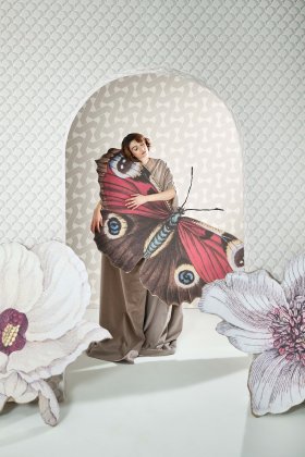 donna che tiene una farfalla gigante in mano in mezzo a due fiori giganti su sfondo di carta da para