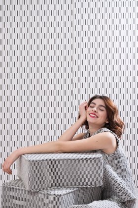 Ragazza appoggiata a un pouf cubico vestita con lo stesso pattern geometrico della seduta.