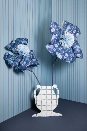 un vaso di cartone con dei fiori giganti di carta nell'angolo di una stanza rivestita di carta da pa